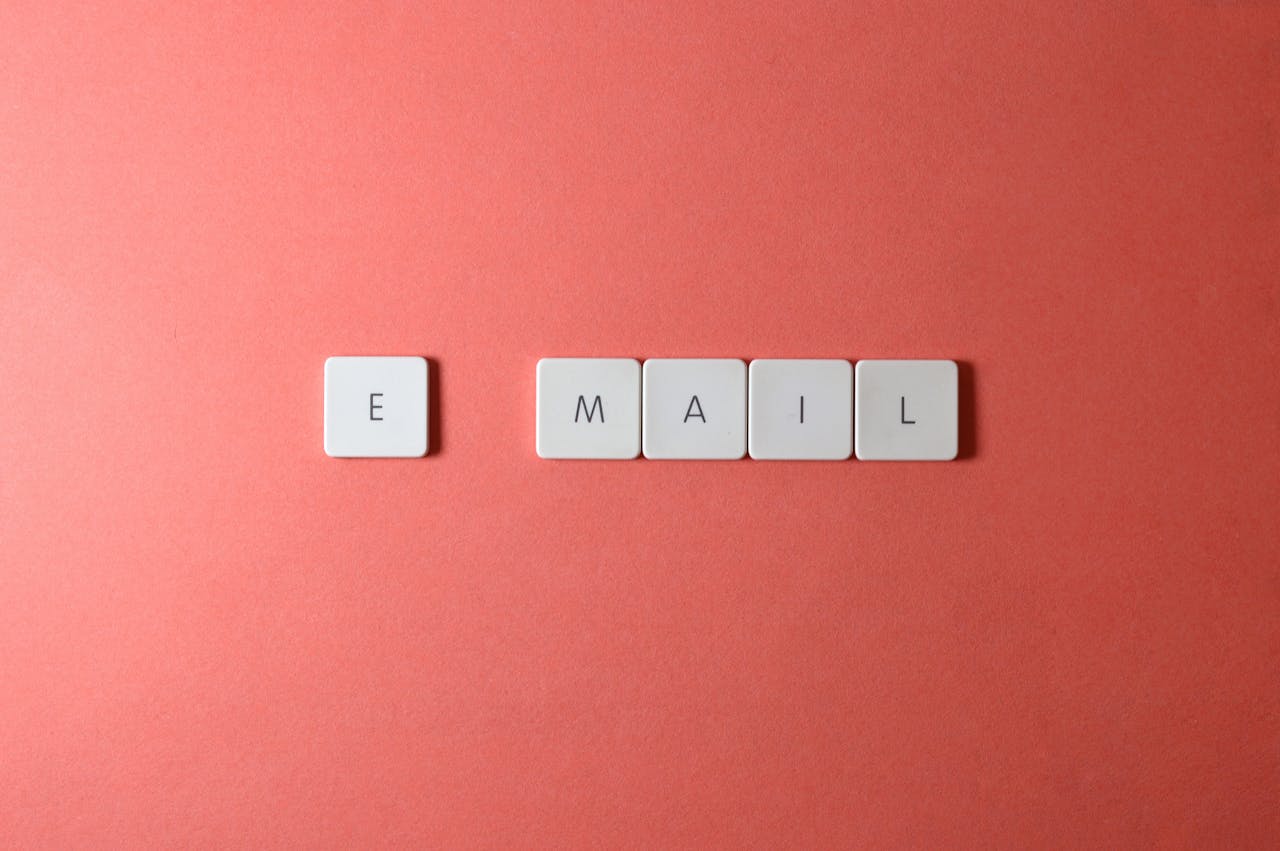 about-01 Flat lay of keyboard letter tiles spelling 'email' on coral backdrop.