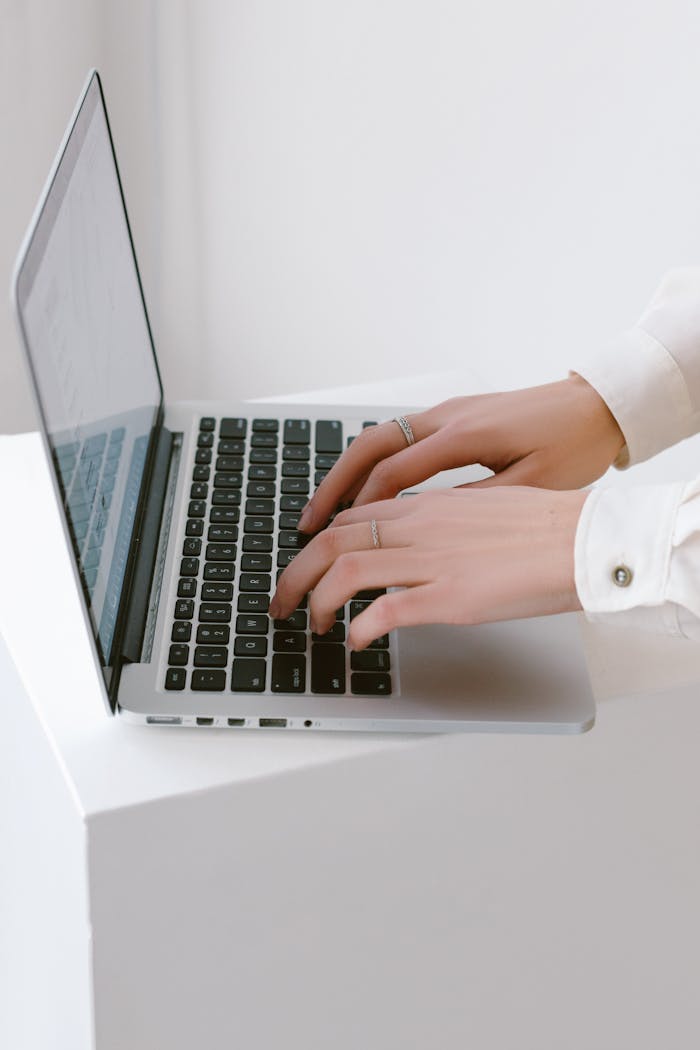 gallery-4 Close-up of hands typing on a laptop in a bright, minimalist indoor setting.